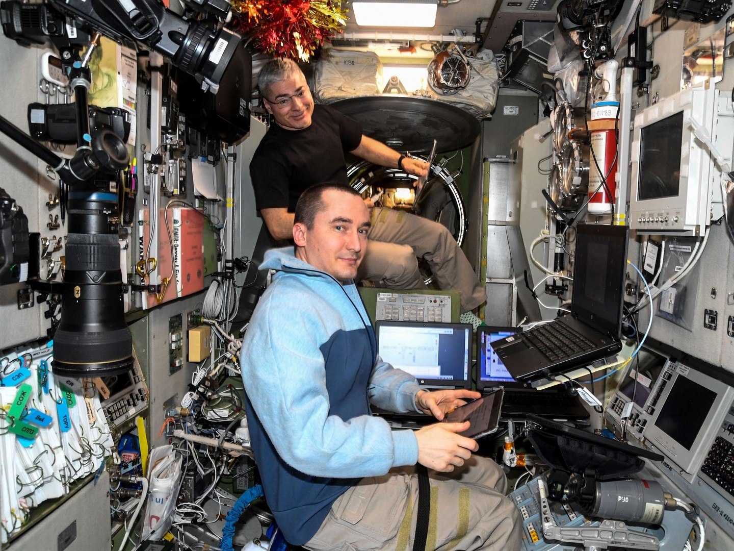 Mark Vande Hei (background) and Pyotr Dubrov train on a computer aboard the International Space Station, on December 28, 2021. Roscosmos/NASA