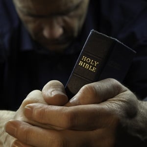 Man praying holding a Holy Bible from Shutterstock