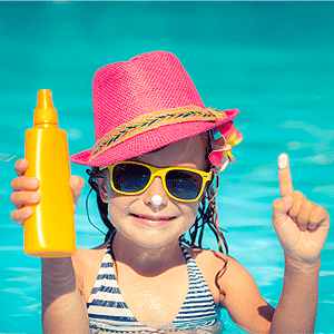 Happy child holding sunscreen lotion in hand, summer vacations concept