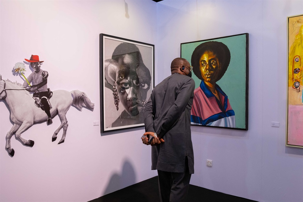 Art enthusiasts look at an artwork by Barry Yusufu titled "Home Girl", at the ArtX annual art fair at the Federal Palace Hotel, Victoria Island. Behind him are two pieces by South Africa's Lunga Ntila. (Benson Ibeabuchi / AFP)
