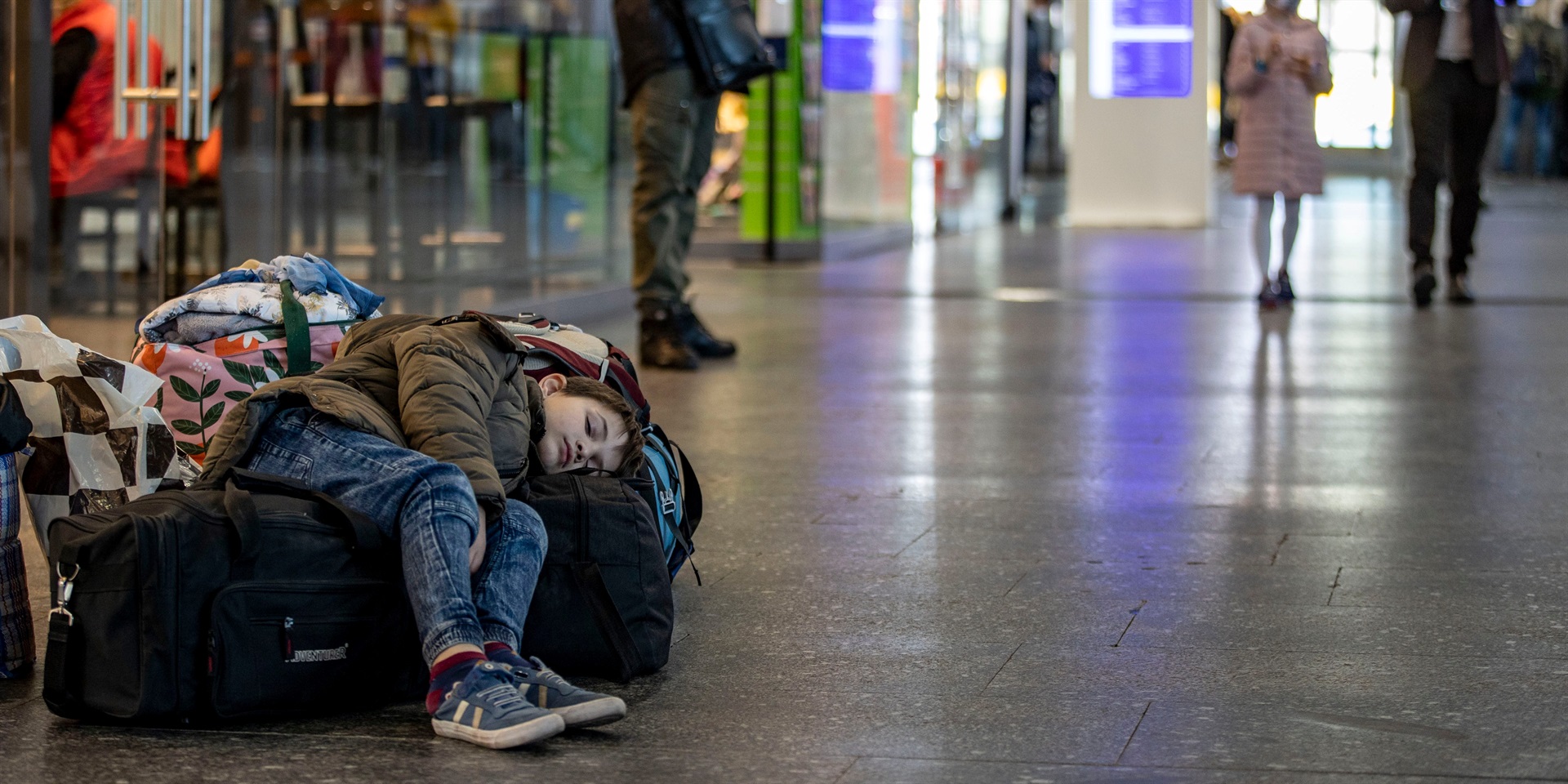 A little boy lies asleep on some travel bags, his mother is looking for ways to continue her journey. Photo by Christoph Reichwein/picture alliance via Getty
