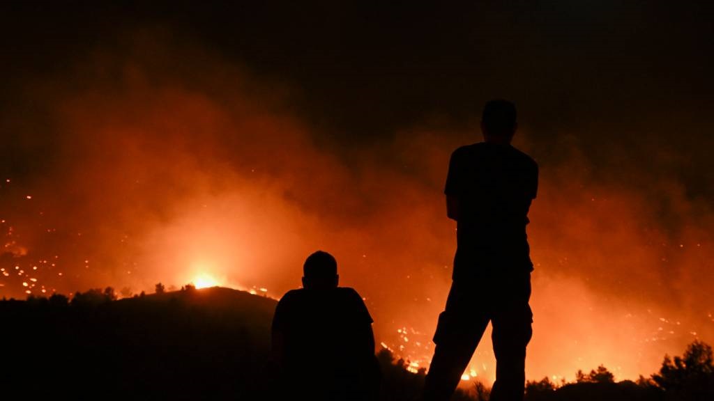 People watch the fires near the village of Malona 