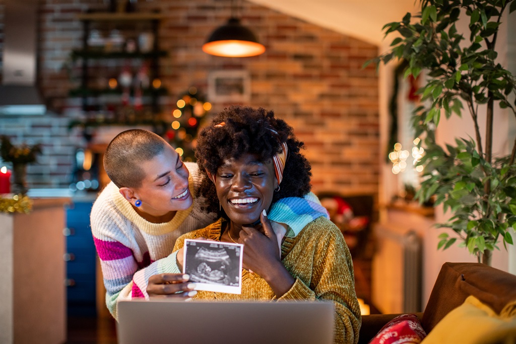 Close up of a young female couple showing off their pregnancy scan to their family over a video call