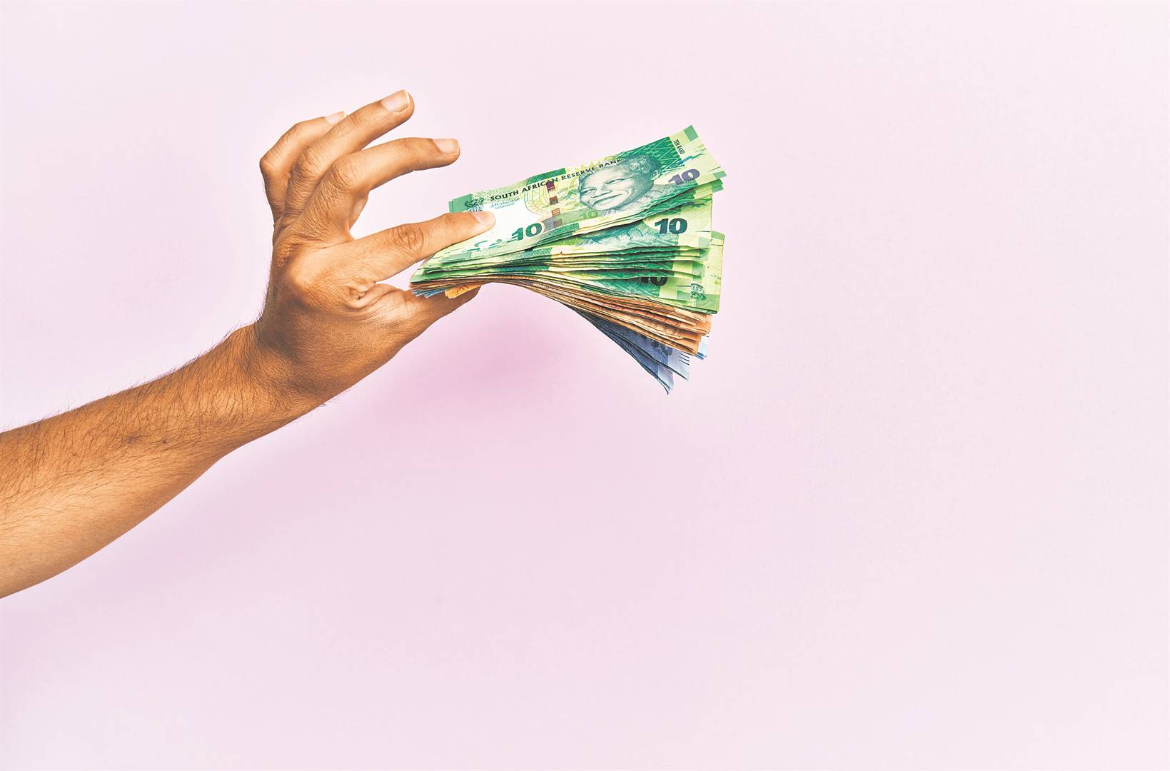 Thata Mina Hispanic hand holding south africa rands banknotes over isolated pink background. Photo: istock 