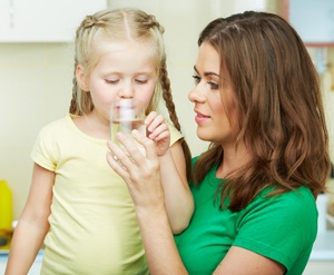 Little girl drinking water in kitchen with young mother from Shutterstock