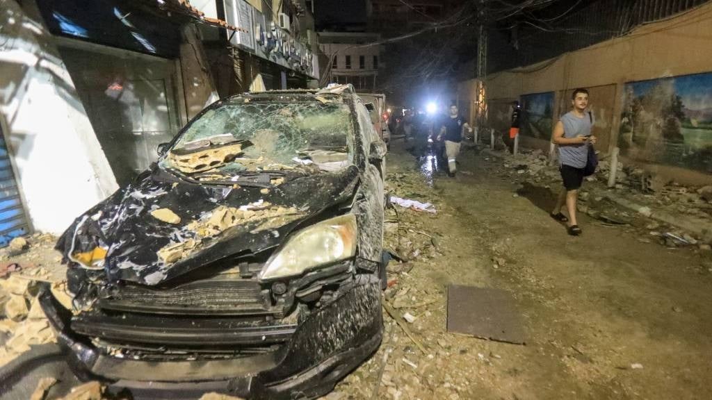 Men walk past debris and a destroyed car after the