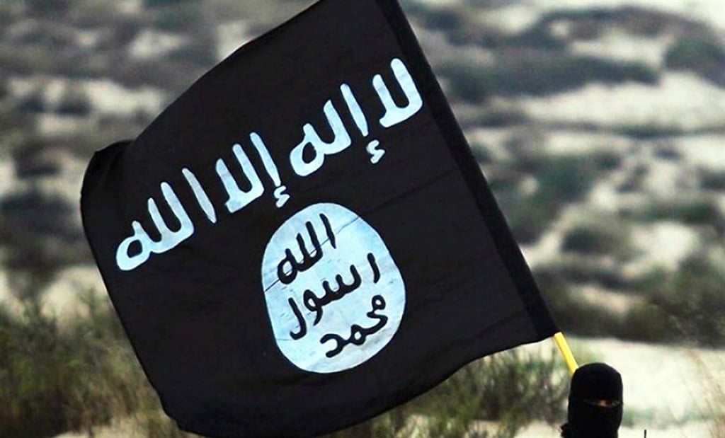 Un soldado del Estado Islámico enmascarado posa mientras sostiene la pancarta de ISIL. 