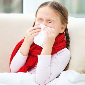 Little girl with flu wearing a scarf and blowing her nose.