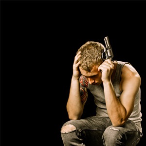 Teenage male holding handgun to head depicting the teen suicide depression concept.