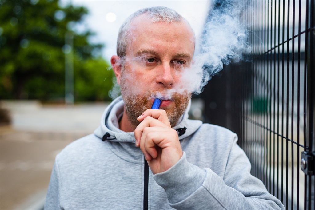 Color image depicting a mid adult man in his 30s vaping using a disposable vape outdoors. Room for copy space.