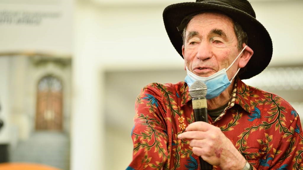 Albie Sachs wearing black hat and face mask down around his chin