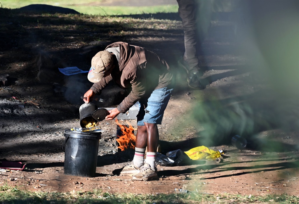 A homeless man prepares breakfast in a park at the corner of St Andrews and Queens Road in Parktown. Photo by Morapedi Mashashe