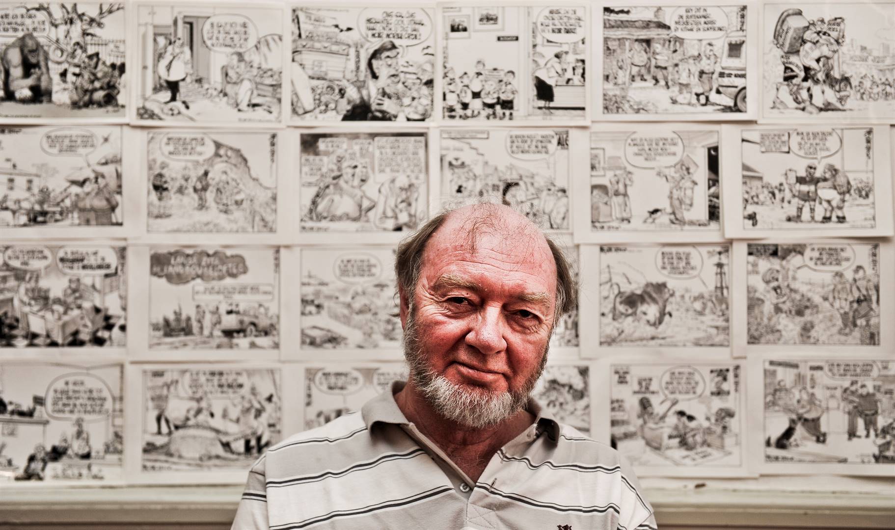 Die ikoniese spotprentkunstenaar Fred Mouton by die KKNK in 2015 met van sy spotprente agter hom. Foto: Jaco Marais