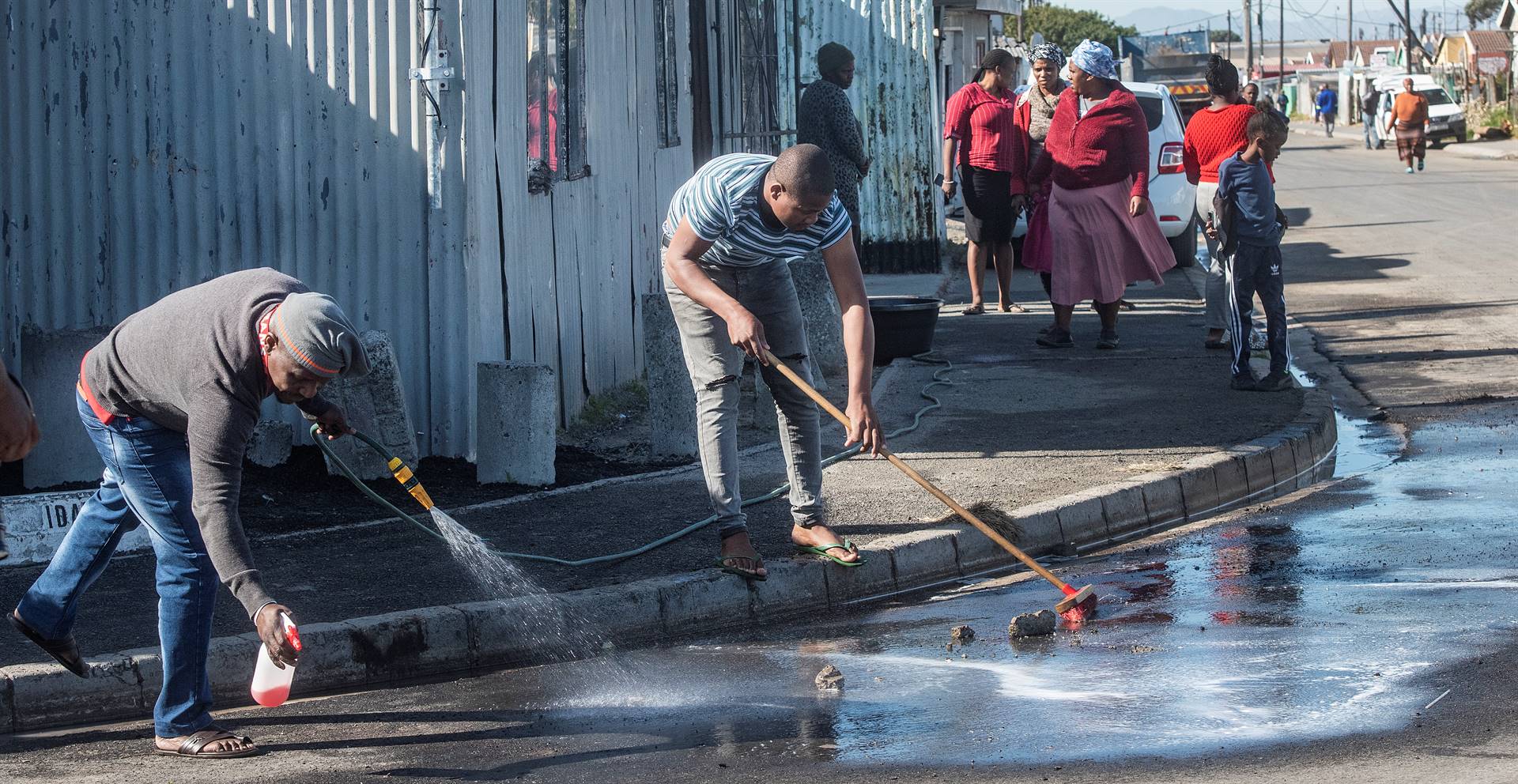Khayelitsha residents cleaning a street where five bodies with bullet holes were found.