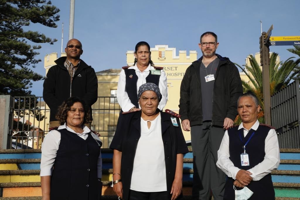 Sr Diane Seale stands with part of the team that supported her. Back Row: Mr Beven Mashedi - Facilities Manager (left); Sr Diane Seale - Operational Manager (Centre), Professor Roger Dickerson - Head of Emergency Centre (Right); Front Row: Ms Vanessa van Wyk - Operational Manager, Medical Ward; Ms Salama Basardien - Nursing Deputy; Ms Ohlen Ohlson - Operational Manager, Surgical Ward.