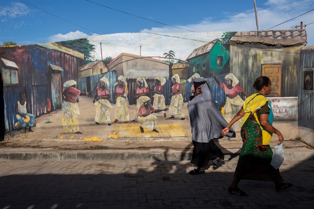 Two women walk in front of a mural with traditional drawings depicting the culture and history of the Mafalala neighbourhood in Maputo on April 21, 2022. 