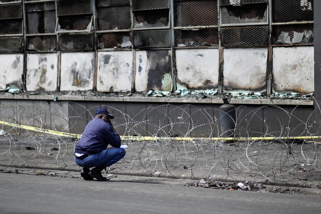 A South African Police Service officer kneels at the scene of a burned apartment block in Johannesburg on September 1, 2023. 
