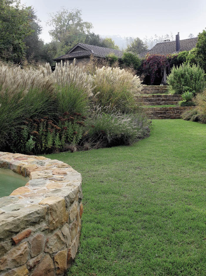 Ornamental grasses are at their most breathtaking in late autumn when their  graceful plumes dance gently in even the slightest breath of wind. Natural stone steps and a stone wall around the edge of the pool blend in beautifully with the grasses in this garden.