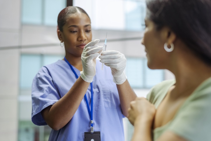 A black female nurse flicks a syringe before injec