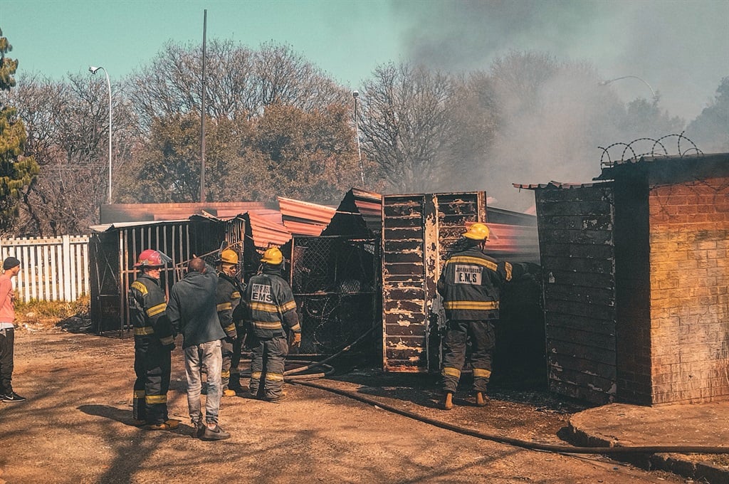 A resident talks to firefighters outside a garage where two vehicles were destroyed in Vrededorp, Johannesburg.
