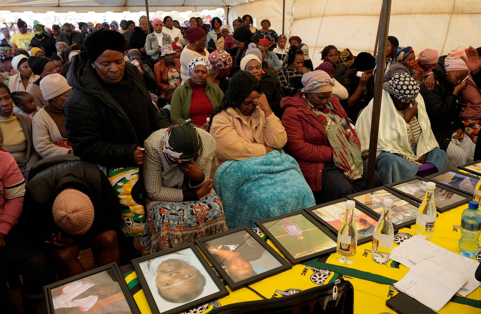 Families members sit in front of displayed photos of their deceased relatives during a memorial service for the 16 victims of the Nomzamo tavern attack , in Nomzamo Park, Soweto, South Africa, Thursday, July 14, 2022. South Africa is reeling in shock from a spate of weekend bar shootings in which armed men burst into three taverns and opened fire indiscriminately, killing people. Photo: AP Photo/Themba Hadebe