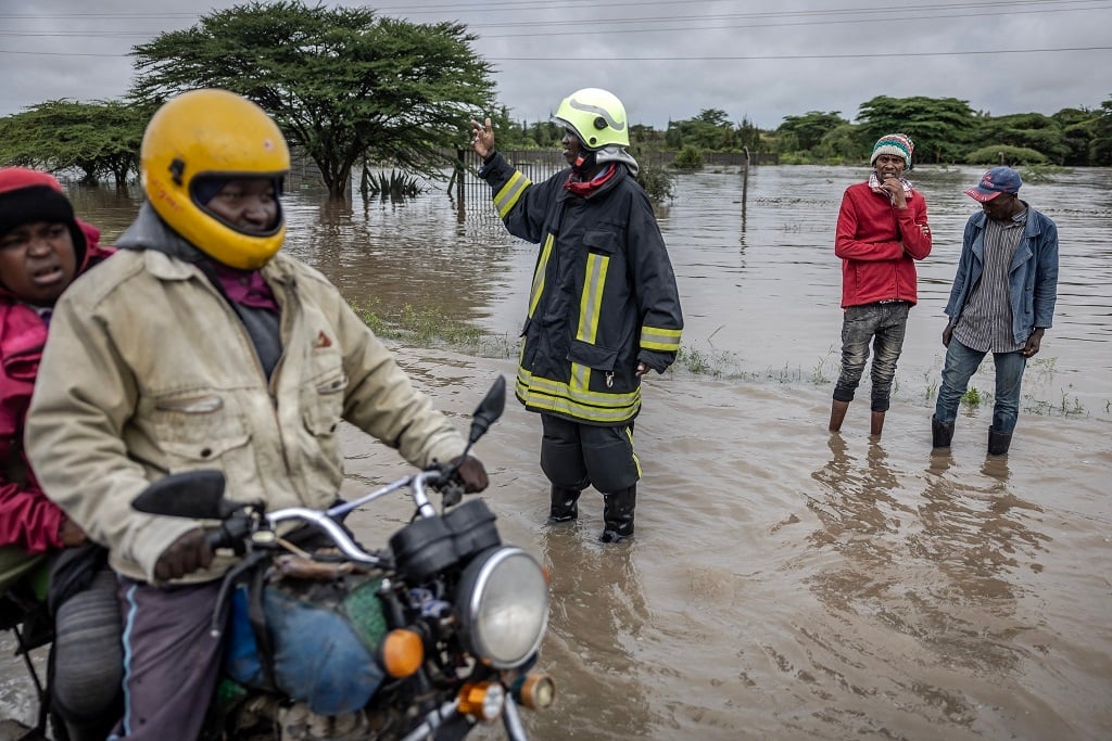 A Kenyan firefighter gives directions to commuters as residents inspect a road heavily affected by floods following torrential rains in Kitengela, on 1 May, 2024. (Luis Tato/ AFP)