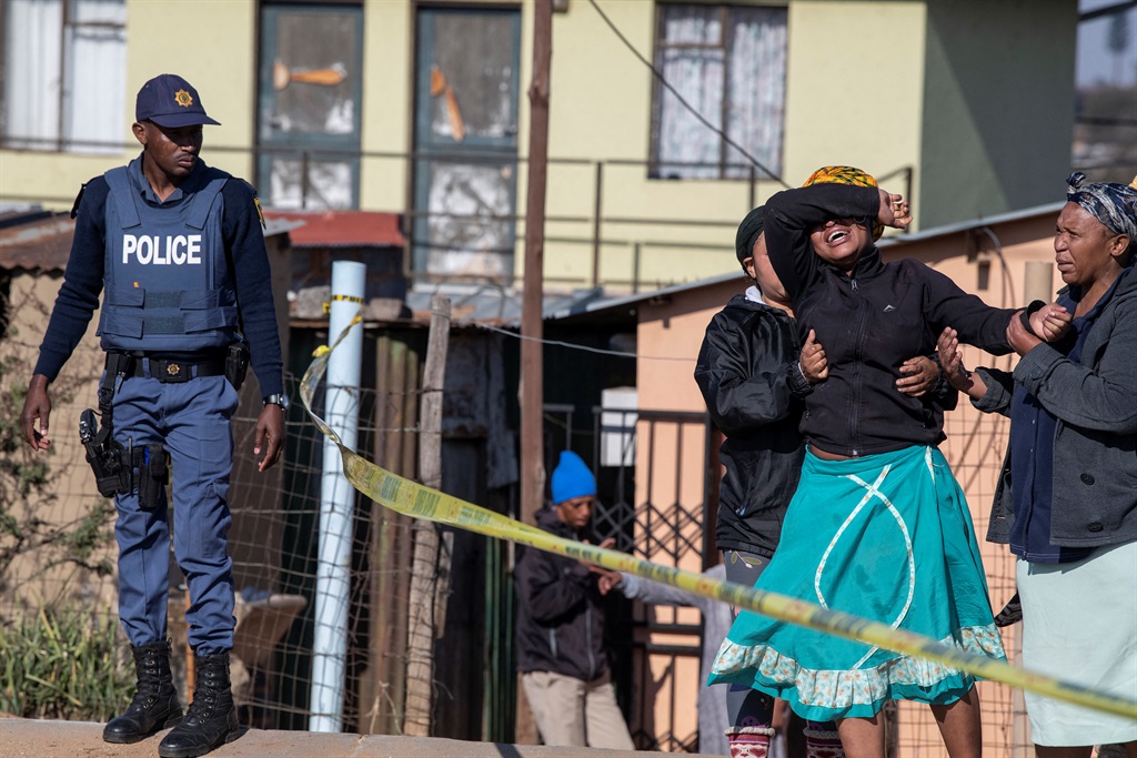 A victim's relative cries as police officers refuse to let her cross the police barrier and enter the crime scene in Soweto. Photo: Ihsaan Haffejee/AFP