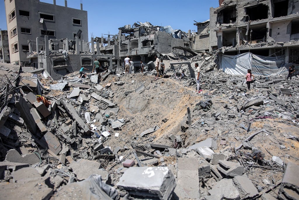 People gather around an impact crater in the aftermath of Israeli bombardment in the Sabra neighbourhood in the south of Gaza City on 27 June 2024 amid the ongoing conflict in the Palestinian territory between Israel and Hamas. (Omar Al-Qattaa/ AFP)