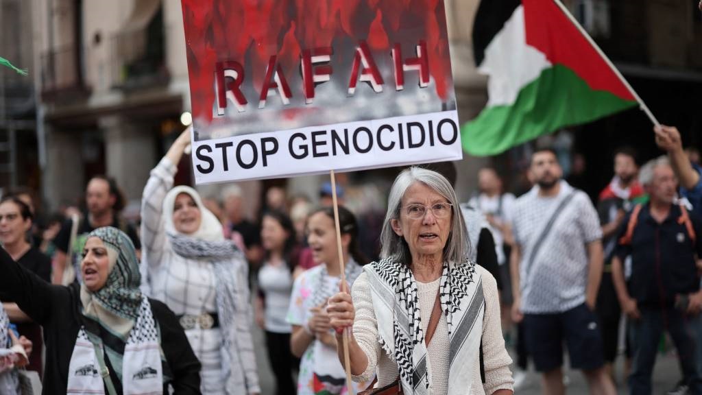 A protestor holds a sign reading 'Rafah, Stop geno