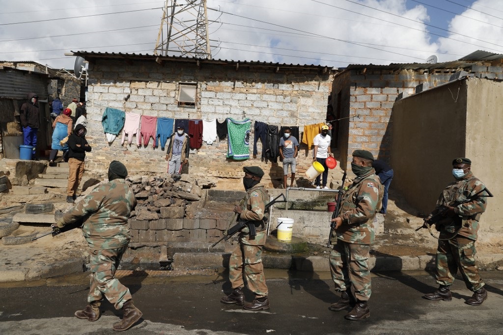 People stand near their homes and watch as members of the SANDF patrol their area in Alexandra township, Johannesburg.