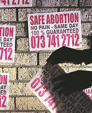 A man plasters posters on the wall offering "Safe Abortion" in Mthatha, South Africa. (Picture: Bonile Bam, Gallo Images)