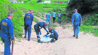 Cops cover Nkululeko Mzobe’s body after digging it up from a shallow grave on the beach in Hibberdene. 