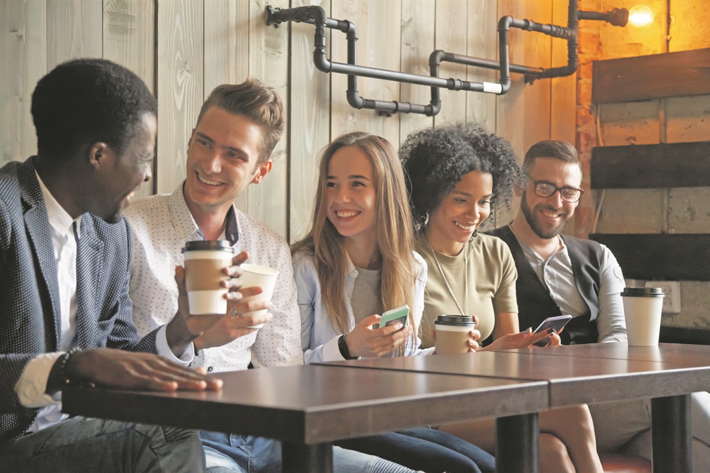 plugged in Happy multi ethnic group of friends talking using smartphones in cafe, diverse young people laughing having fun at coffee break in coffeehouse, cheerful millennials enjoying meeting in coffeeshop
