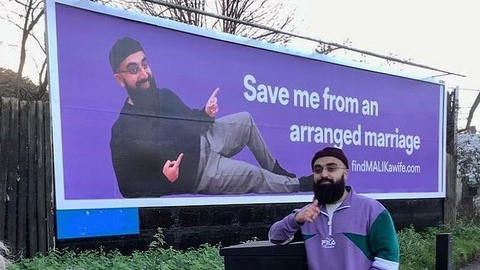 Malik stands next to his billboard in London. Image via @findmalikawife/Instagram
