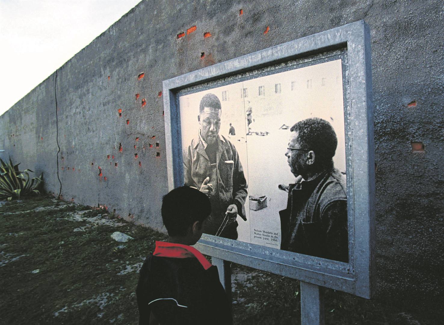 A young boy stands in front of a plaque in the main courtyard area of the prison on Robben Island. Photo: Antoine de Ras