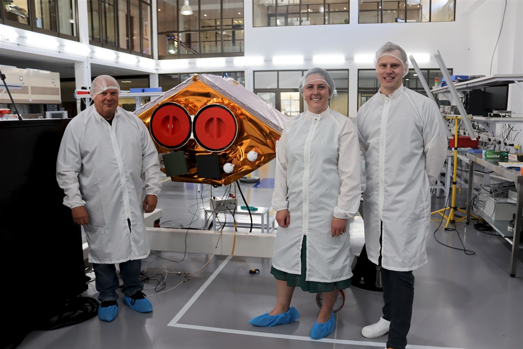 Van links staan mnr. Schalk Olivier, me. Lorita Christelis en mnr. Kannas Wiid by die Agrisat-1, die grootste satelliet wat Suid-Afrika nóg gebou het, asook die eerste ter wêreld wat op die landbousektor gaan konsentreer.