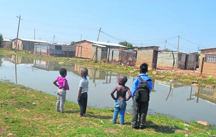Children stand next to a lake of sewage in Jouberton.            Photo by Mohanoe Khiba