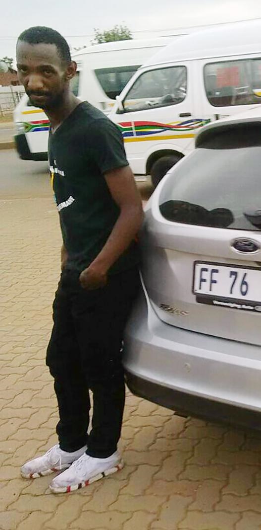 An apparently drunk Thabo Rakhale leans against a silver Ford Focus moments after he crashed into it.
