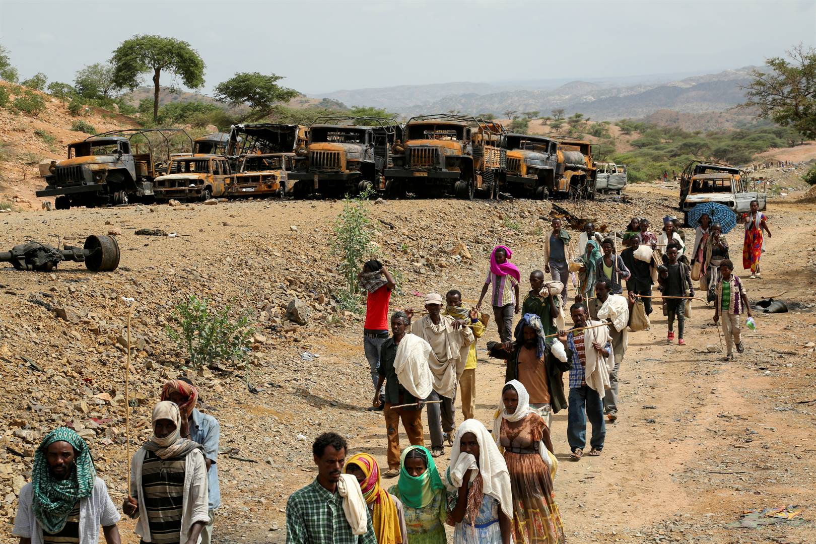 Residents walking back from a market in southern Tigray, Ethiopia, walk past vehicles that have caught fire. Photo: Reuters / Giulia Paravicini