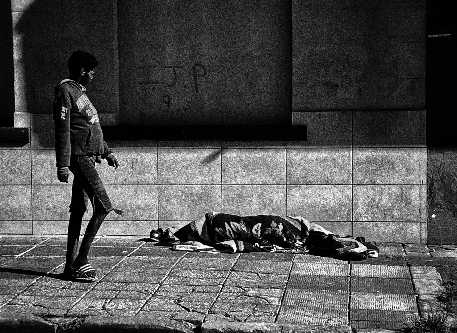 A woman looks at another person asleep on a pavement in downtown Johannesburg