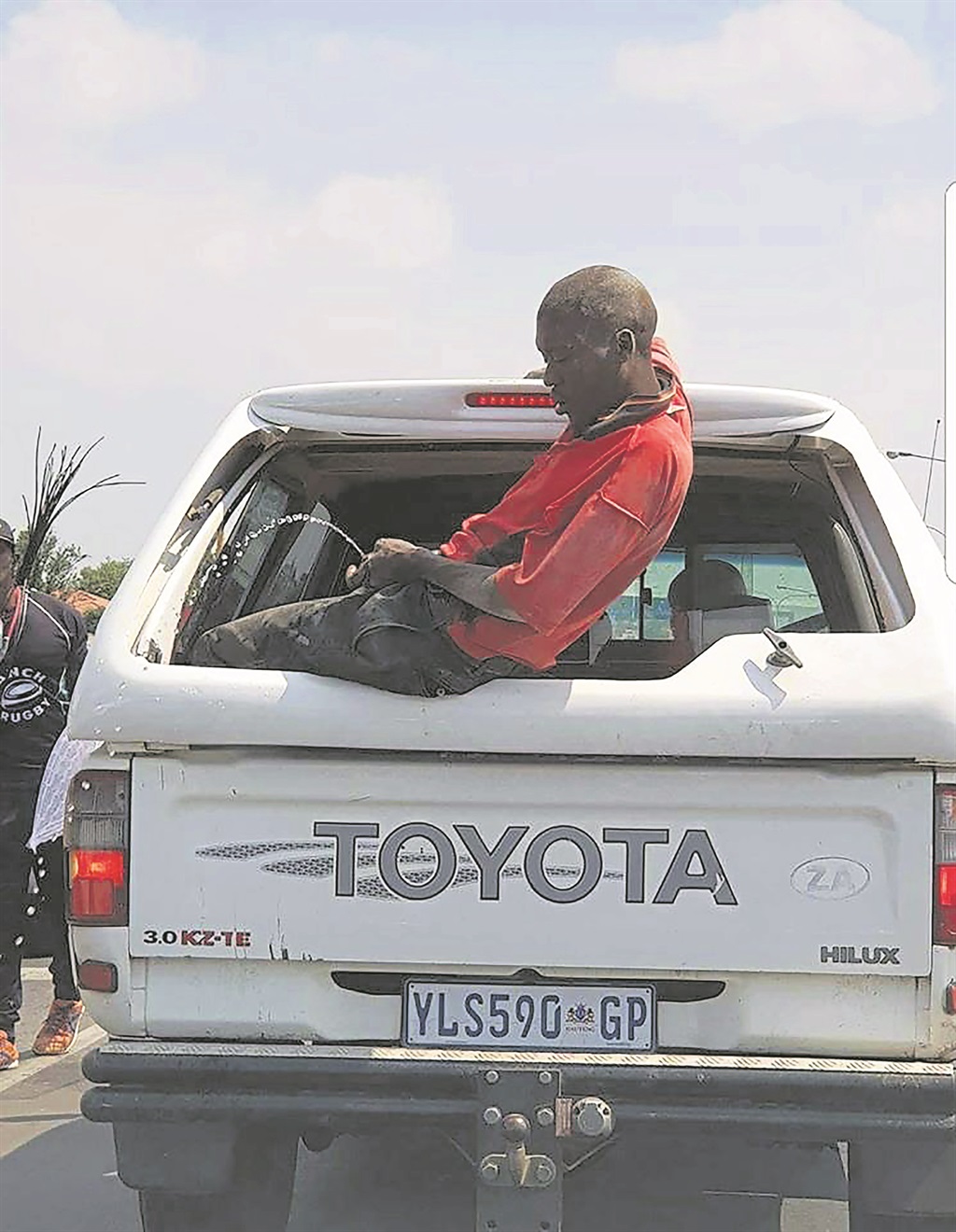 A drunk man urinates from the back of a moving bakkie. 