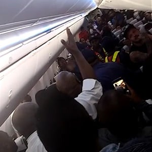 Fellow commuters come to the aid of a passenger being removed from the flight. (Screengrab)