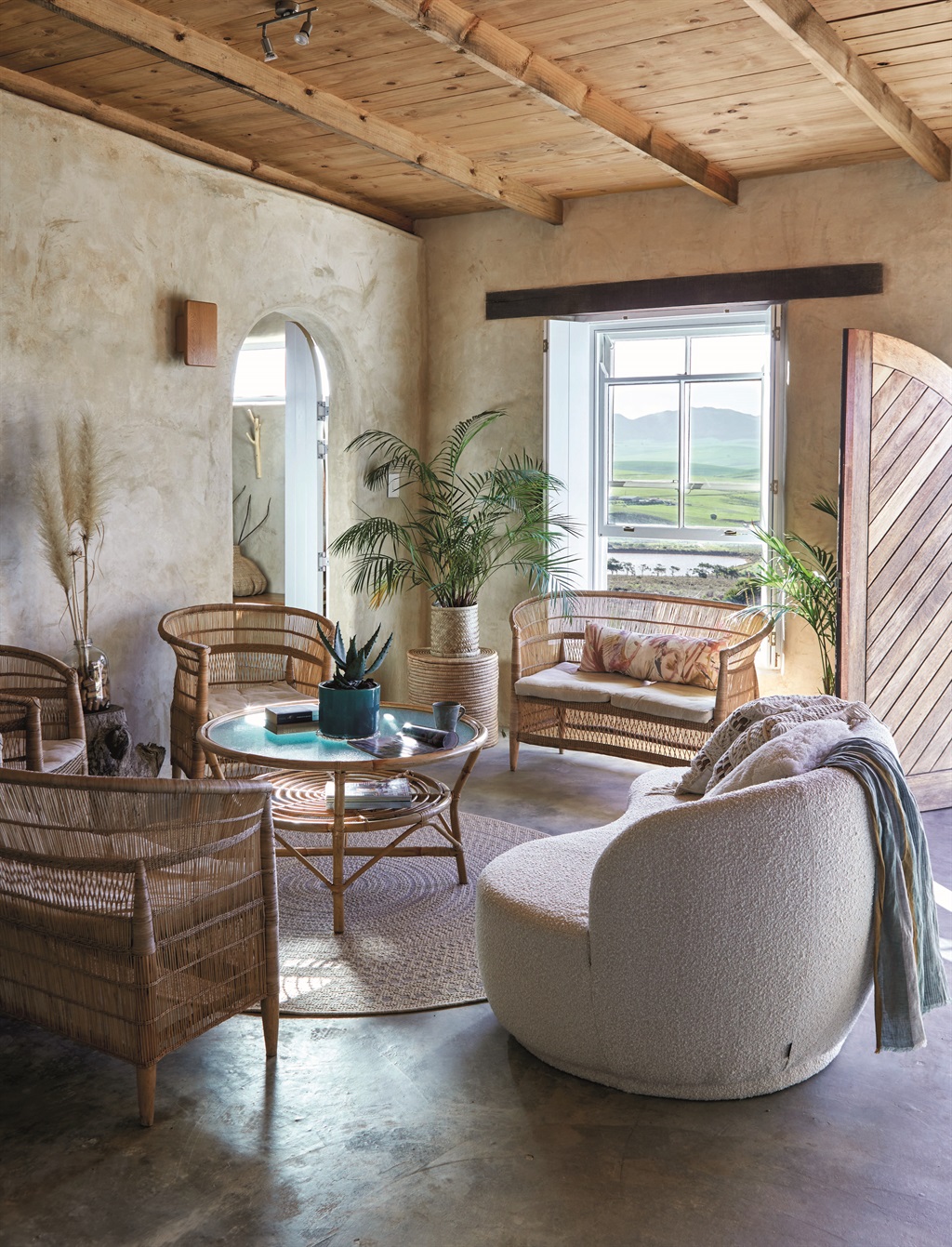 The living room boasts an unobstructed view of the Overberg Valley. The arched doorway on the left leads to the only bedroom. The ceilings were made with sustainably grown pine.
Scarf over sofa from Mungo; sofa from The Sofa Company; round rug from Hertex; rattan table from Mebel