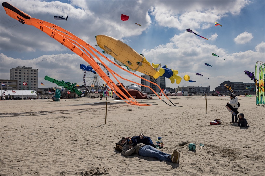 A man lies down on the beach with his son as people fly kites during the 35th International Kite Festival (RICV) at the beach of Berck-sur-Mer, northern France, on April 18, 2023. 