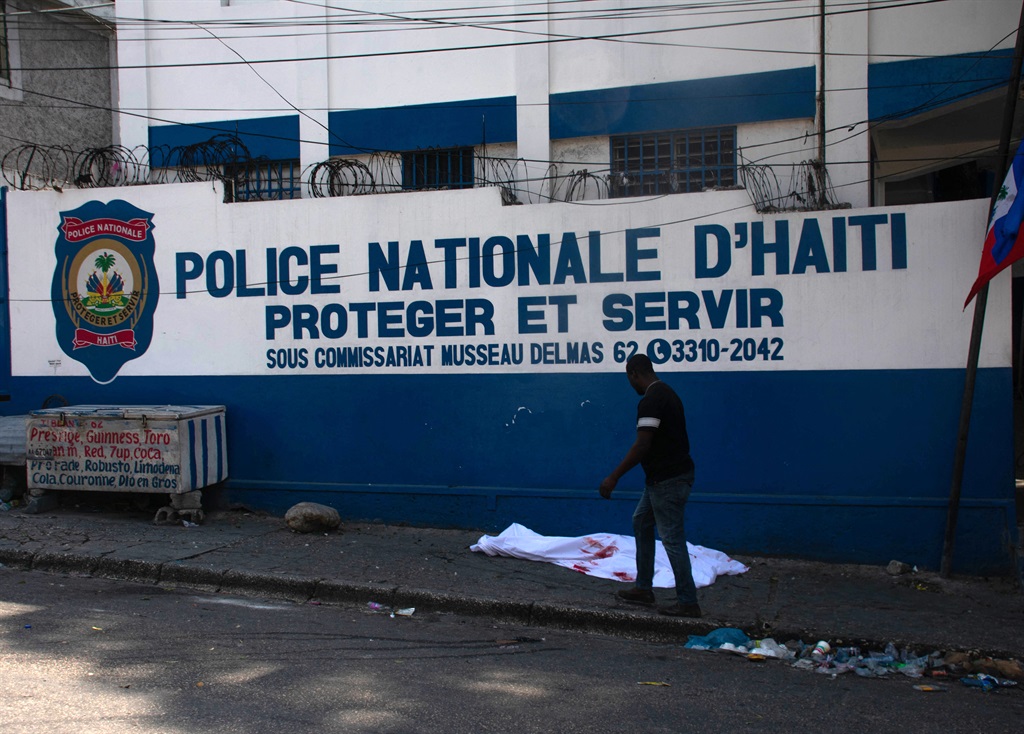 A man walks past the body of a police officer killed amid ongoing gang violence in Port-au-Prince, Haiti, on 20 March 2024. Negotiations to form a transitional council to govern Haiti advanced on 20 March, as the United States airlifted more citizens to safety from gang violence that has plunged the impoverished country into chaos. (Clarens Siffroy / AFP)