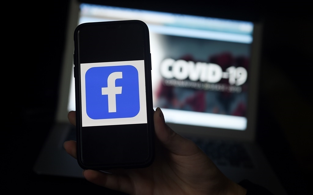 Facebook logo is displayed on a mobile phone screen photographed on coronavirus Covid-19 illustration graphic background.