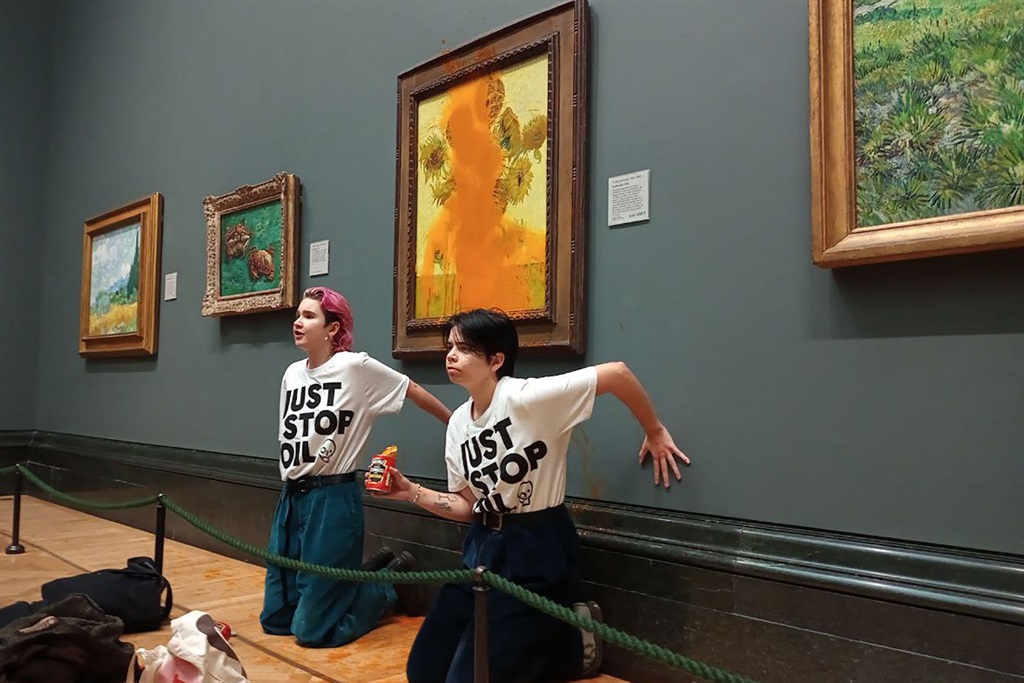 A handout picture from the Just Stop Oil climate campaign group shows activists with their hands glued to the wall under Vincent van Gogh's "Sunflowers" after throwing tomato soup on it.