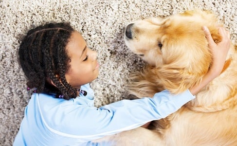 Girl and dog embraced lying on the carpet.