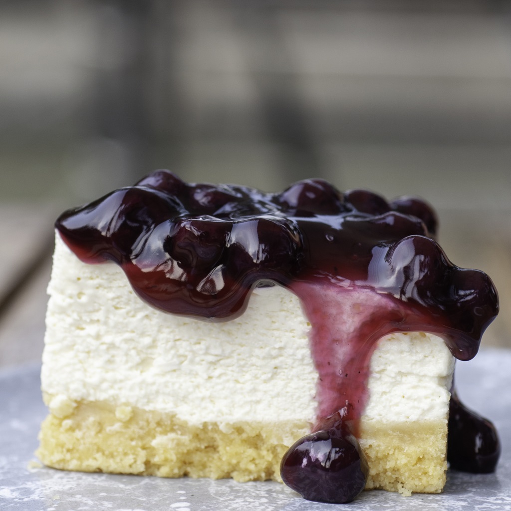 Piece of cheesecake topping with black currant and blueberry sauce serve on white plate. Photo: iStock