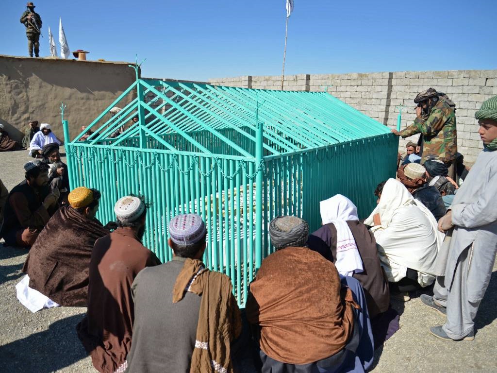 Members of the Taliban sit next to the tomb of lat